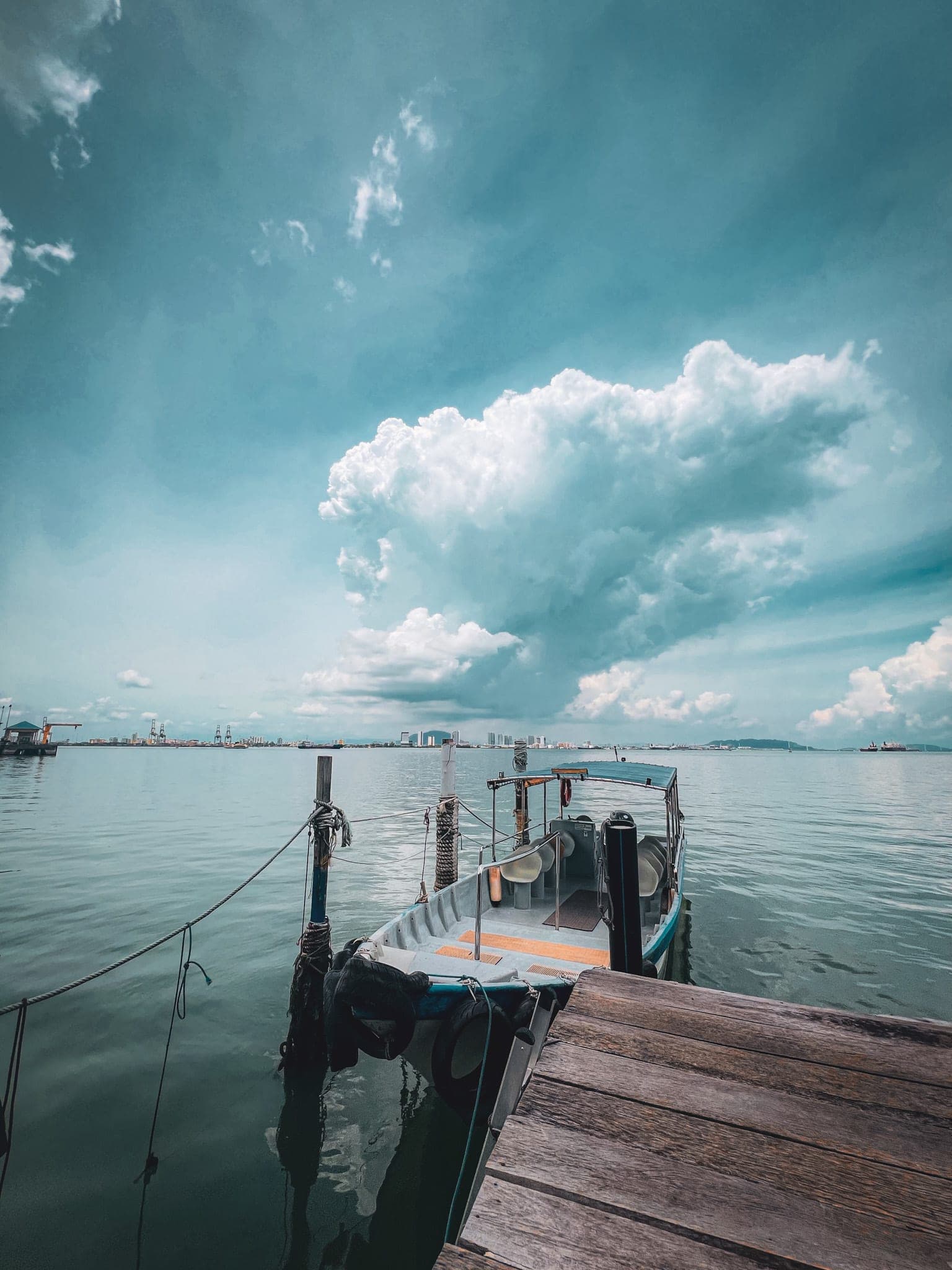 A small boat moored beside a wooden jetty, on calm green water under towering clouds